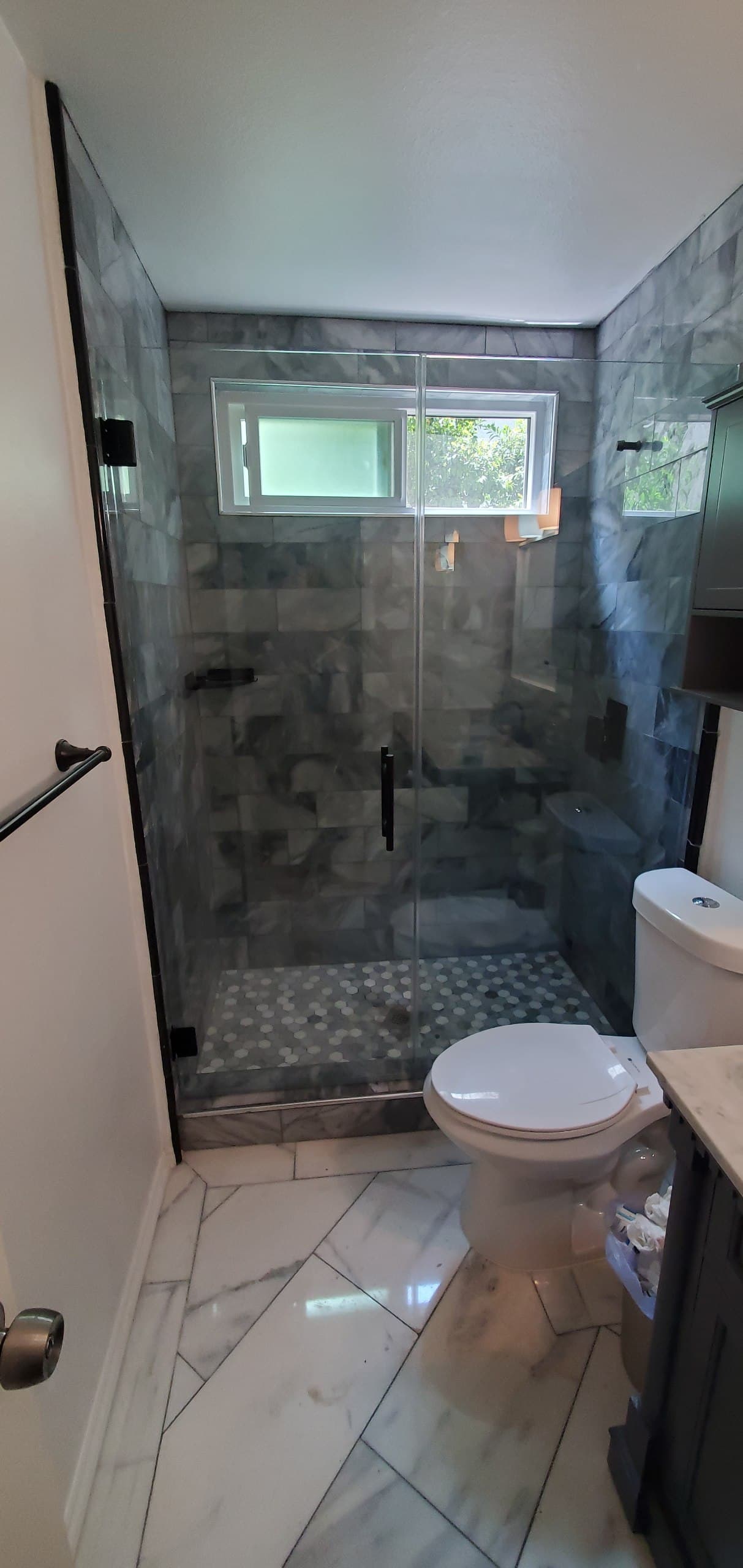 Frameless shower door with black hardware on grey marble tile