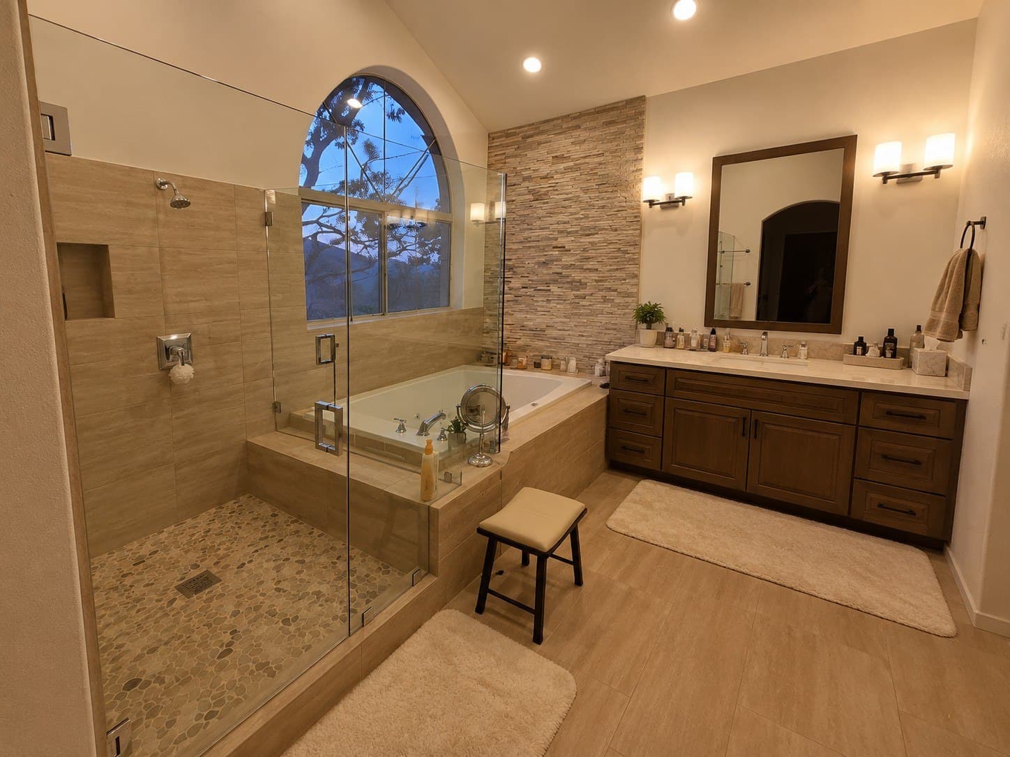 Frameless glass shower enclosure in a travertine master bathroom, beside a soaking tub under an arched window